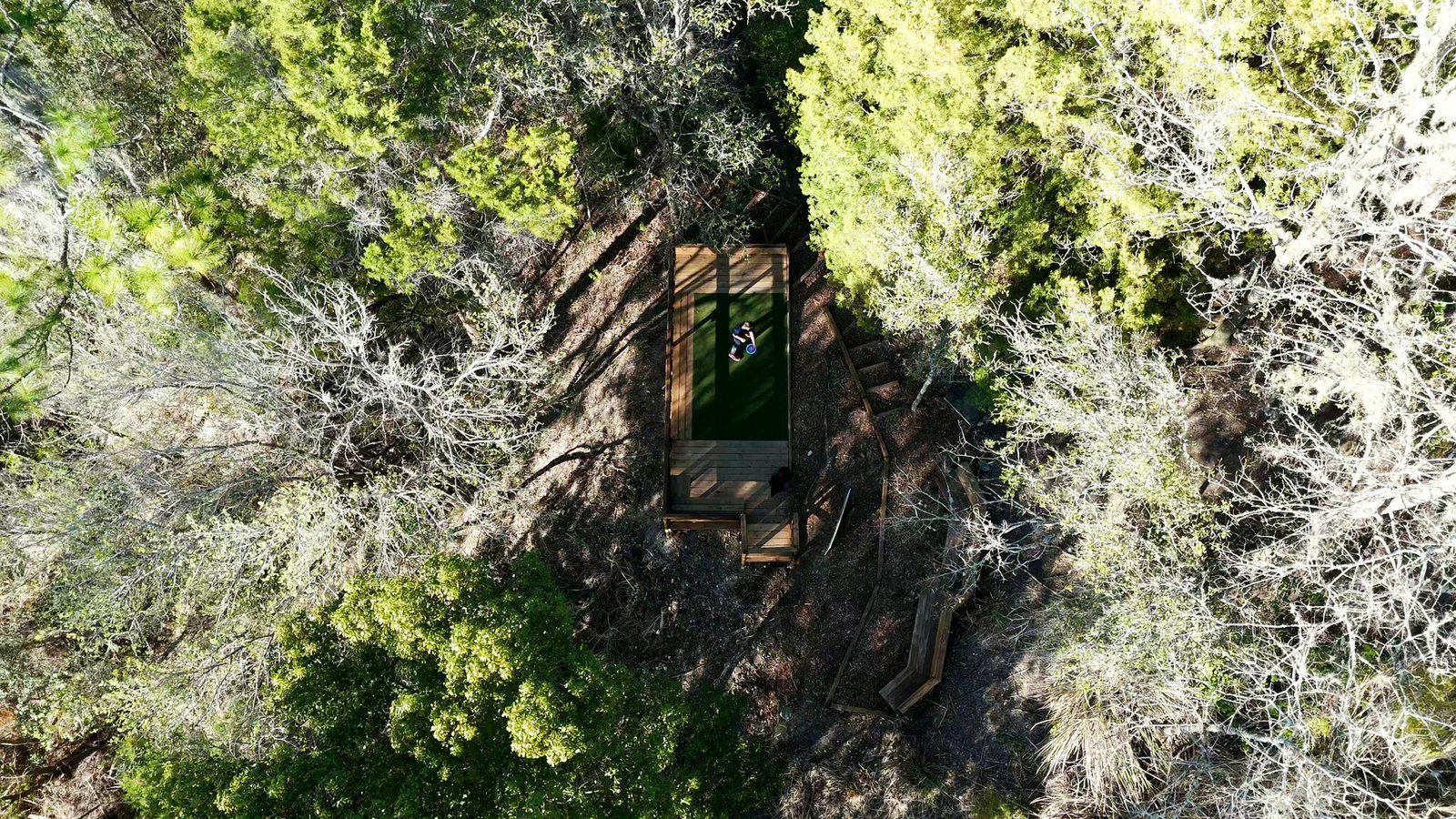 Aerial drone shot of a disc golfer on a wooden tee pad surrounded by Florida pine forest